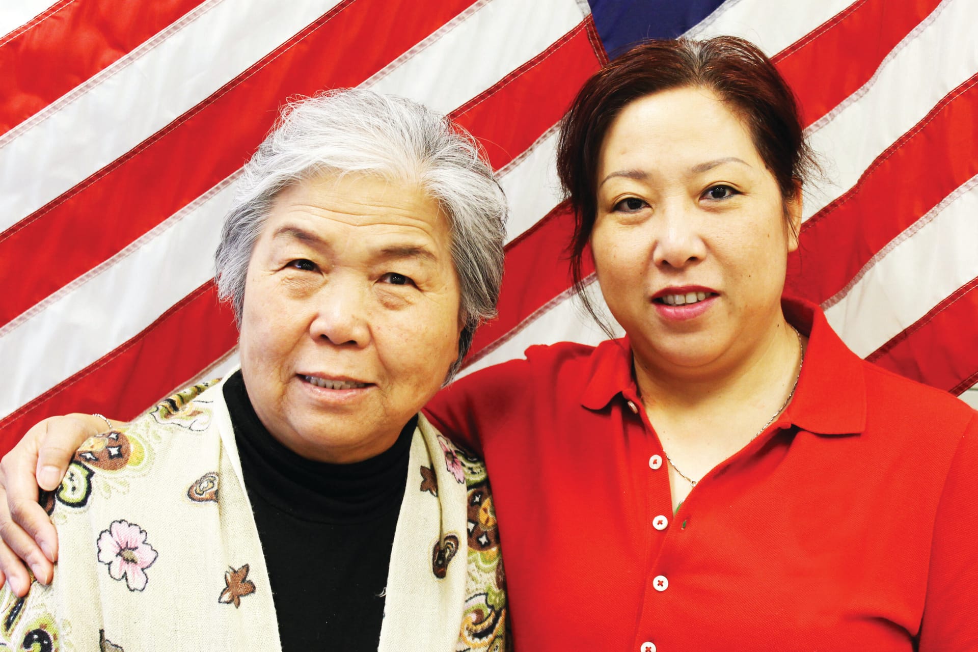 Two women in a citizenship exam preparation class with the American flag in the background.