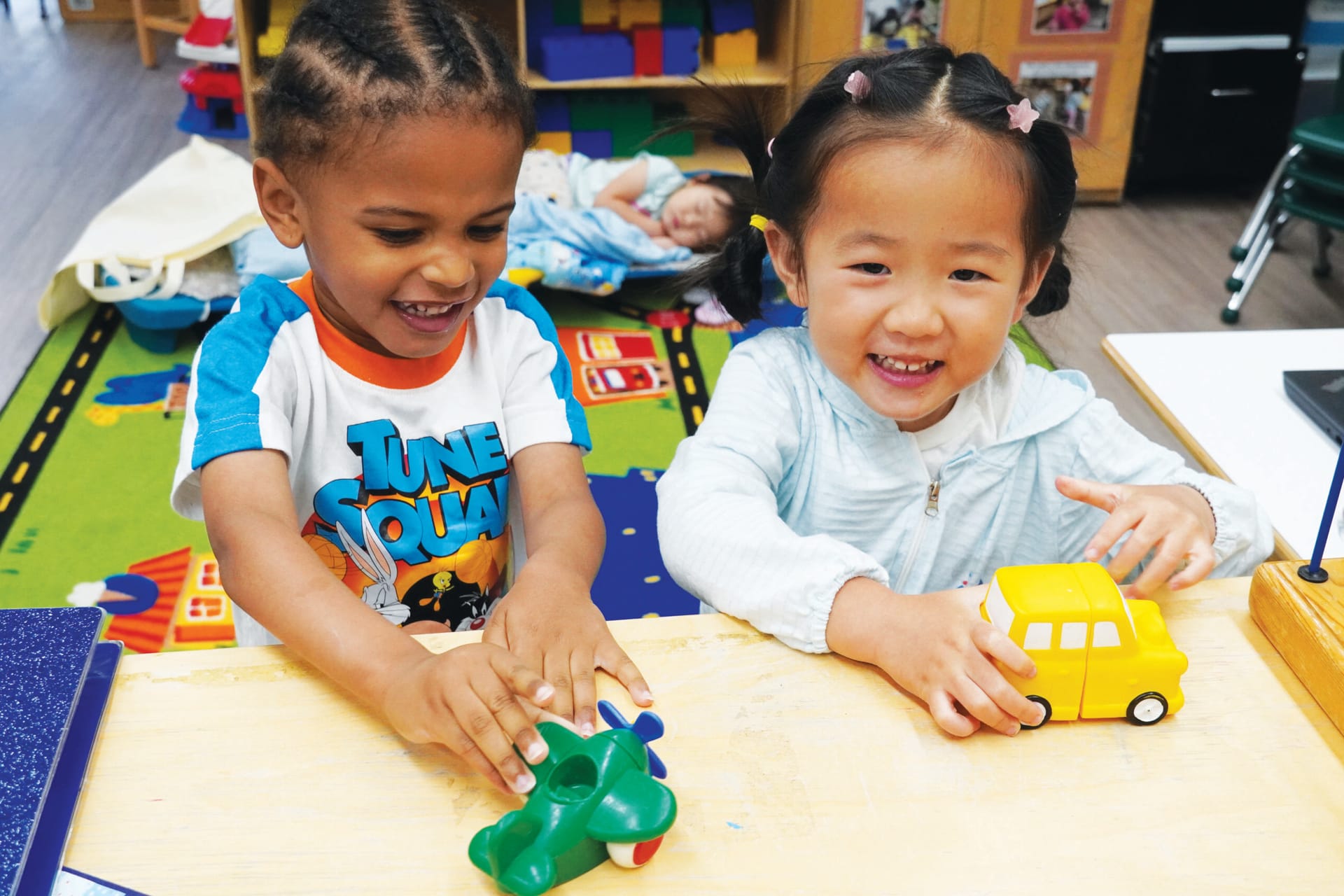 Two giggling little girls playing with toys in a classroom.