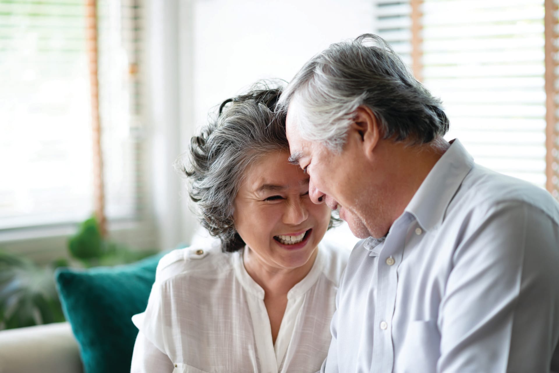 Older Asian couple sitting on couch laughing.