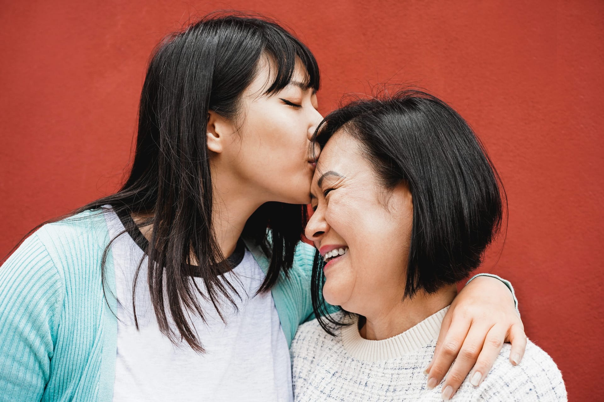 Adult daughter kissing her aged mother's forehead.