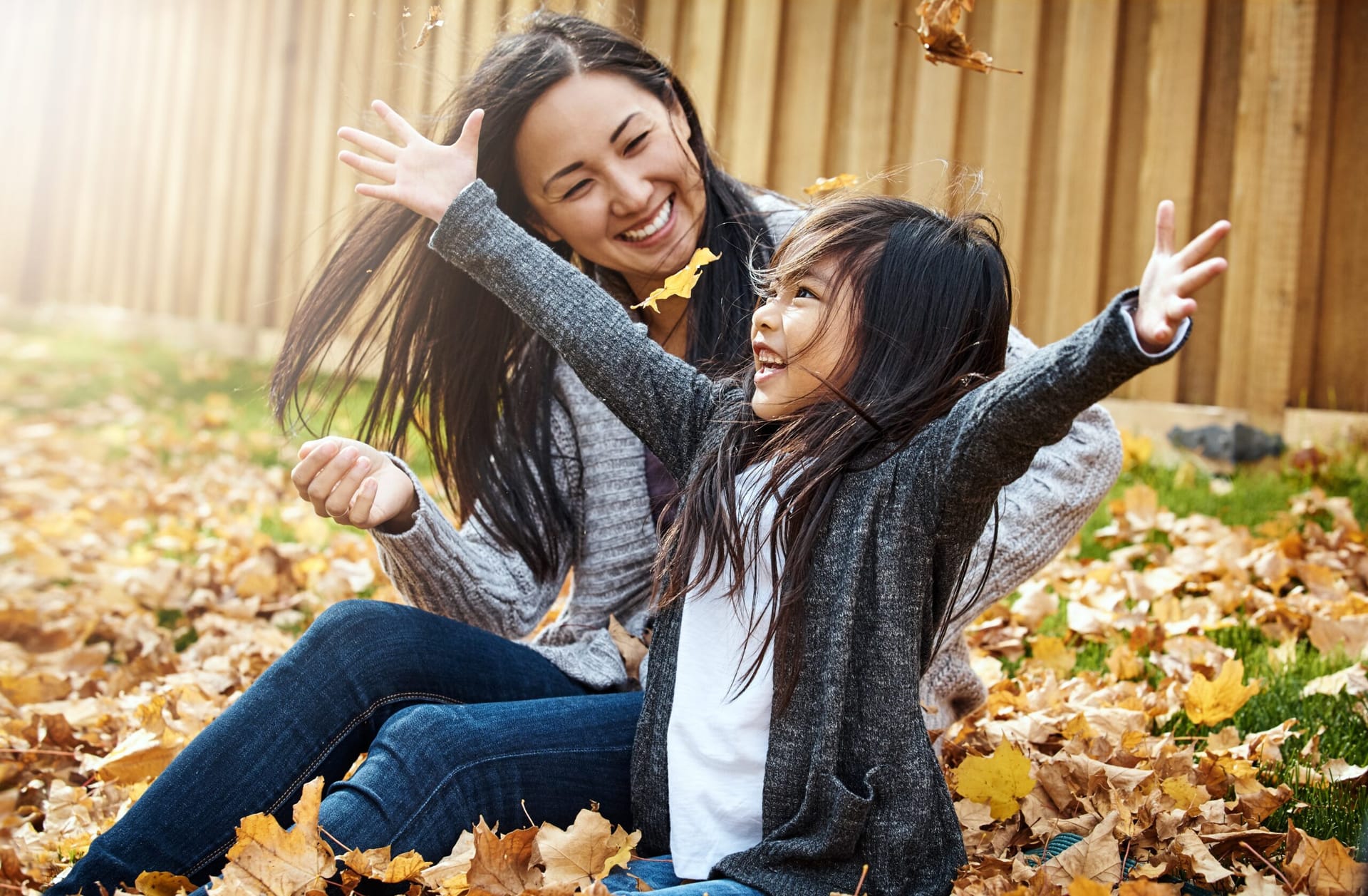 Asian mother and daughter playing in autumn leaves, laughing.
