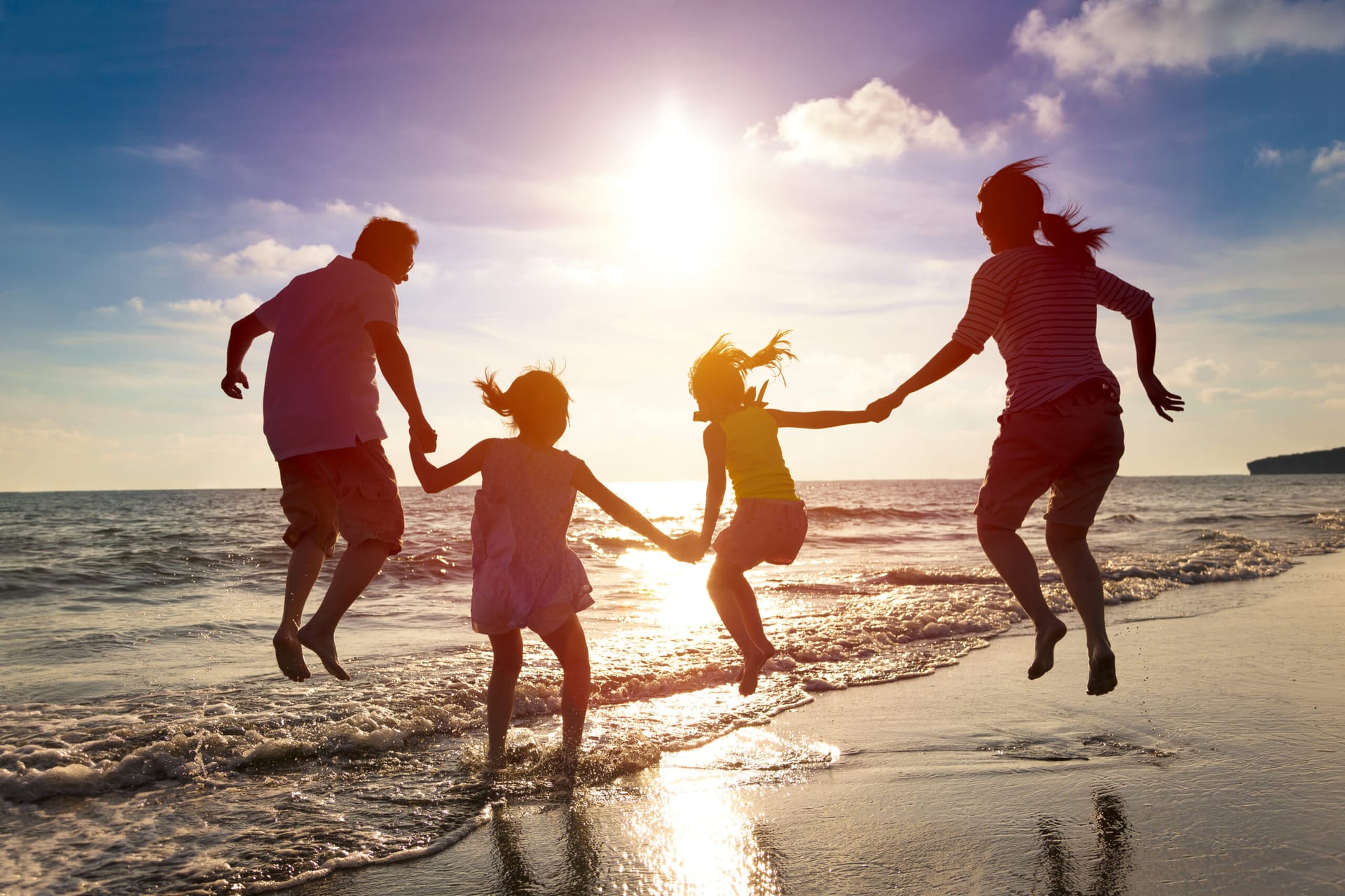 Asian family on the beach, leaping in the air at sunset.