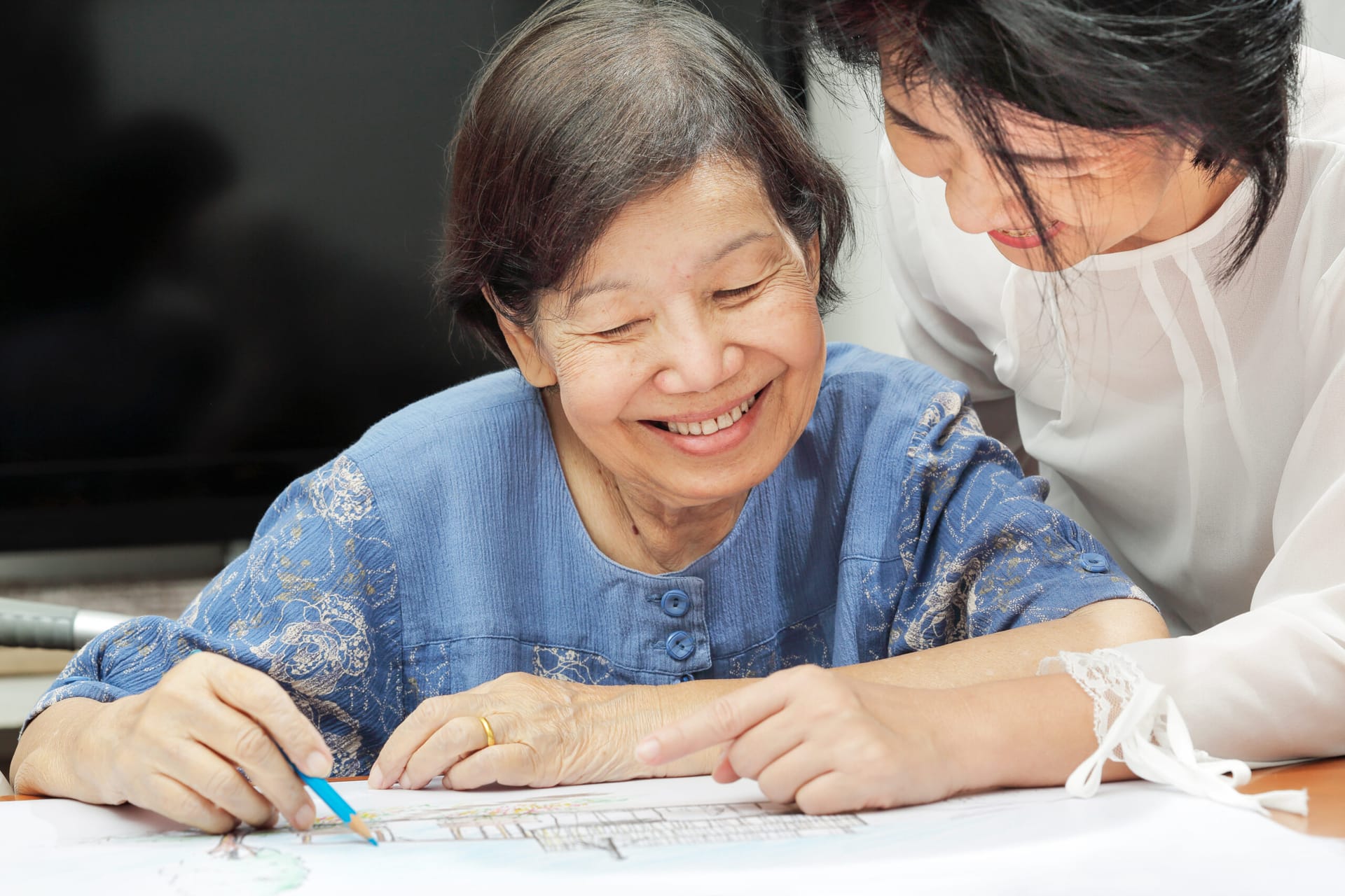 Caregiver assisting older woman with art therapy.