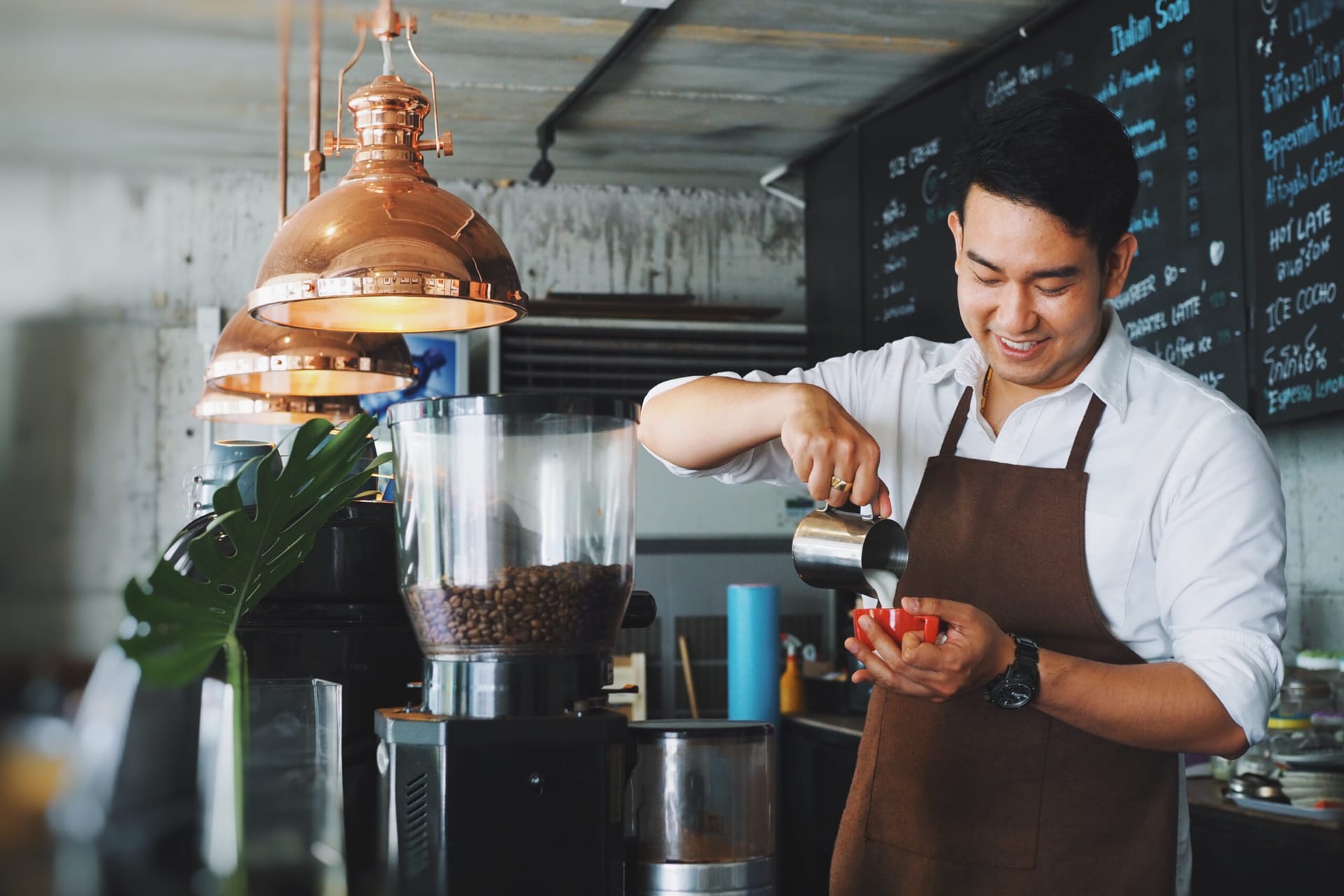 Asian barista pouring cream into coffee