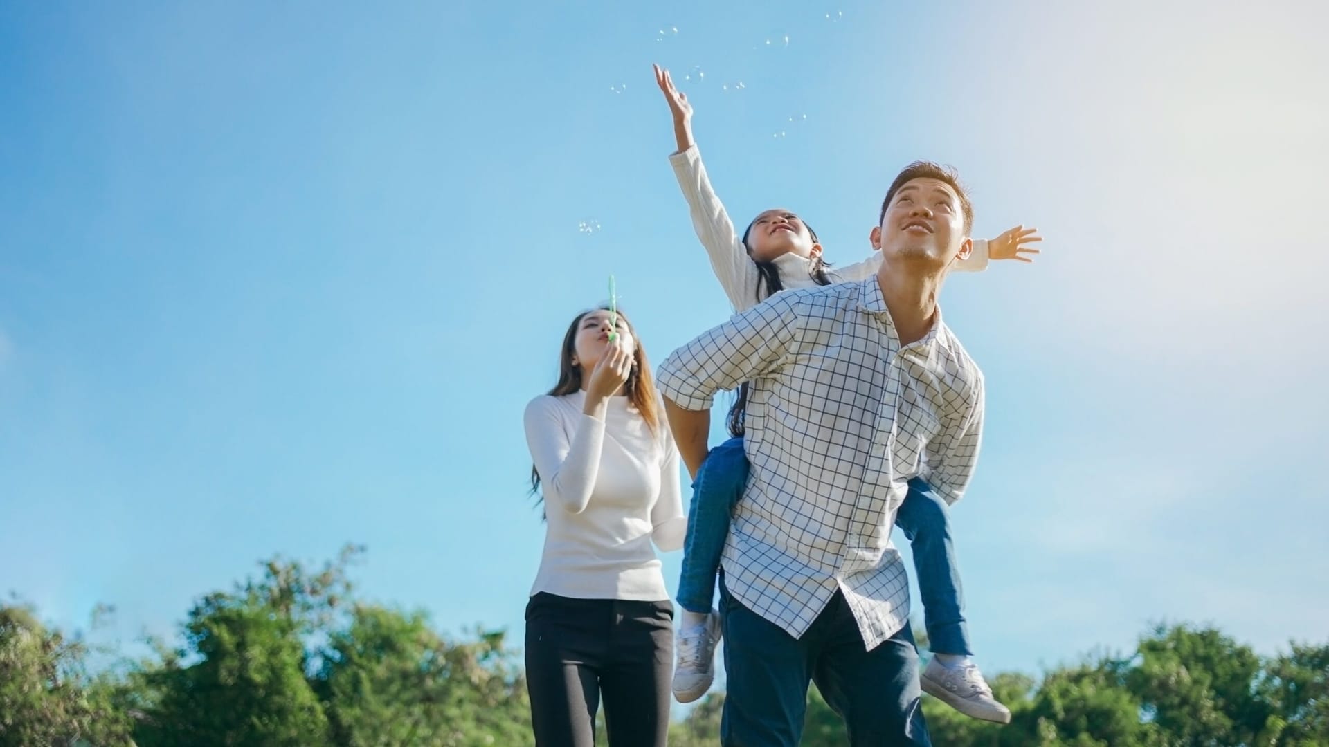 Happy Asian family blowing bubbles against blue sky