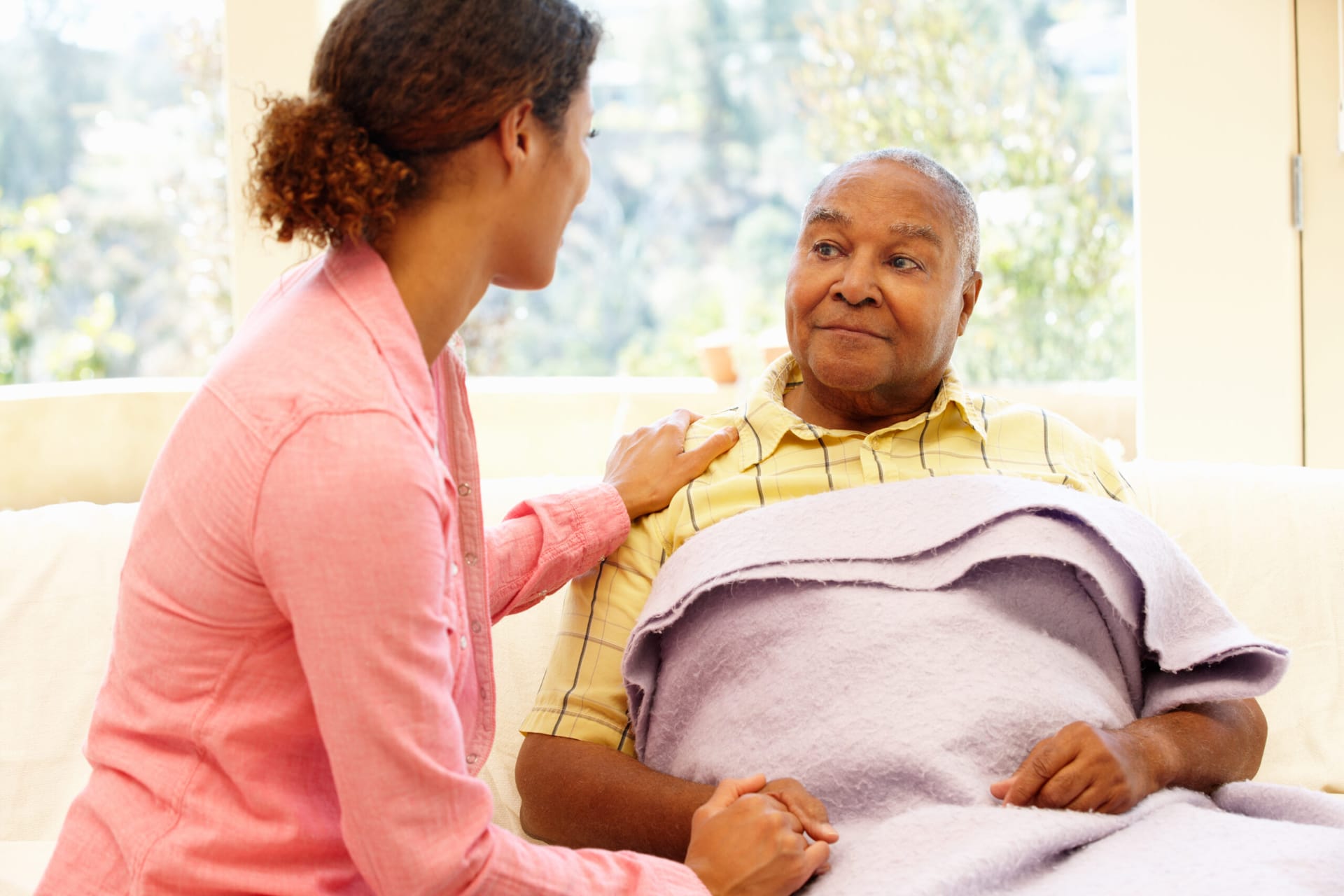 Caregiver looking after older adult man, covering him with a blanket