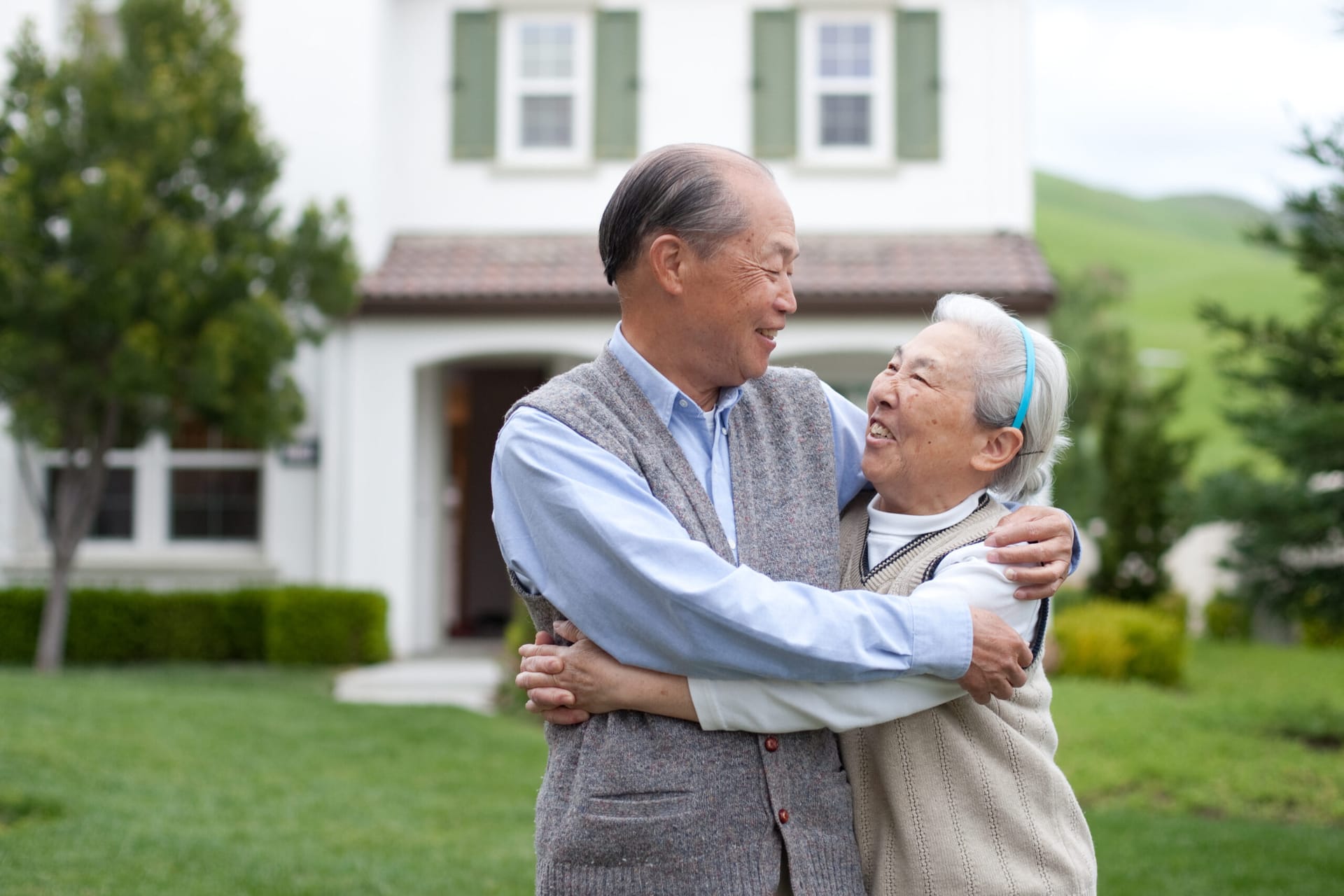 Older Adult Asian couple hugging in front of their house
