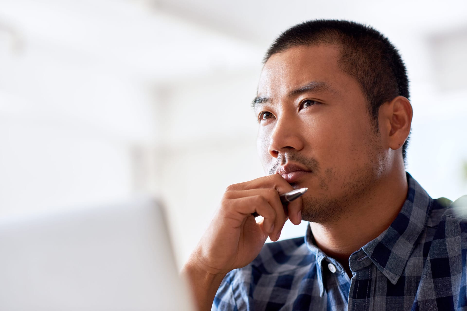 Middle-aged Asian man deep in thought with laptop and pen in hand