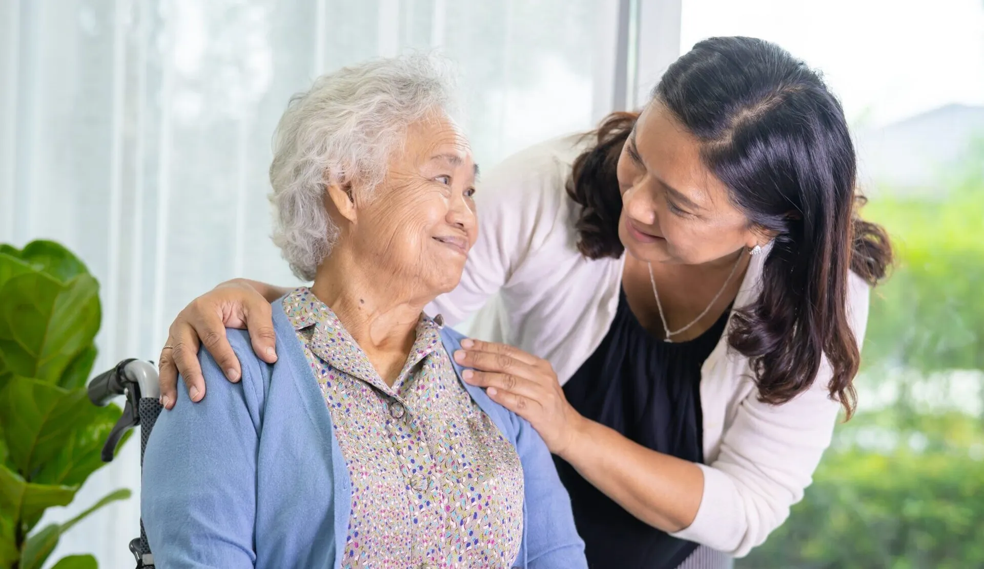 Caregiver smiling at older woman in wheelchair.